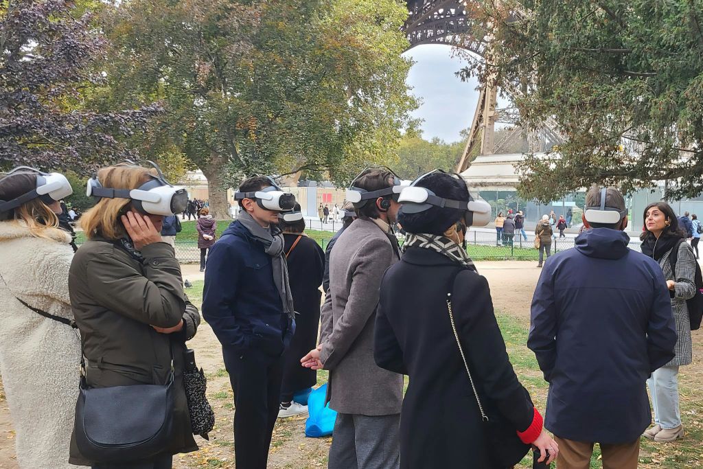에펠탑 근처 공원에 VR 헤드셋을 착용한 한 무리의 사람들이 서서 연설하고 있습니다.