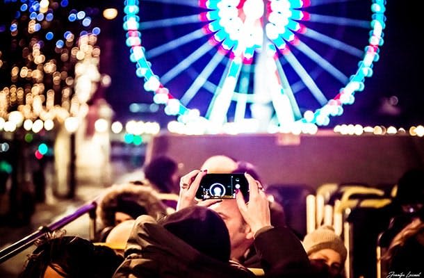 스마트폰으로 사진을 찍고 밝은 빛의 대관람차를 배경으로 한 사람이 밤의 인파에 둘러싸여 있습니다.