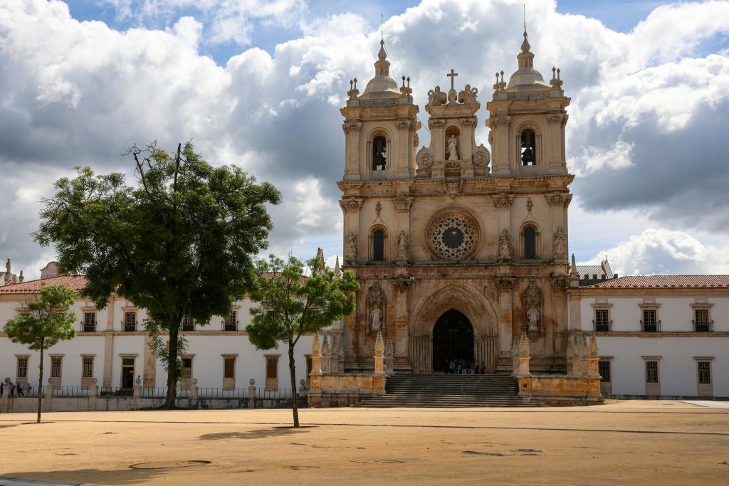 쌍둥이 종탑과 커다란 장미 창문이 있는 역사적인 대성당으로, 흐린 하늘 아래 광장과 나무로 둘러싸여 있습니다.