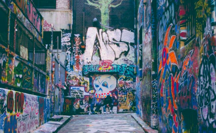 커다란 양식이 돋보이는 얼굴과 다양한 꼬리표를 비롯해 다채로운 색상의 그래피티가 가득한 골목길. 어떤 사람들은 배경에 존재합니다.