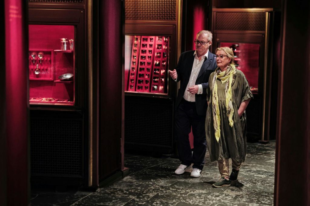 다양한 물품이 전시된 붉은색과 금색의 디스플레이가 어둡게 빛나는 실내를 거닐고 있는 두 사람.