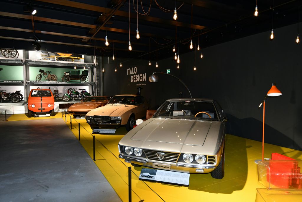 매달린 조명 아래 빈티지 자동차가 전시된 쇼룸으로, 배경에는 'ITALO DESIGN' 간판이 있습니다.