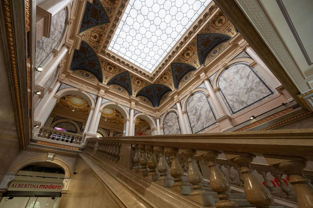 대리석 난간이 있는 화려한 실내 계단, 정교한 디자인의 아치형 천장, 자연 채광이 들어오는 대형 채광창.