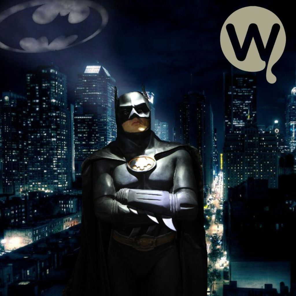 배트맨 의상을 입은 사람이 박쥐 신호와 하늘에 "W" 로고가 있는 야간 도시 풍경에 맞서고 있습니다.