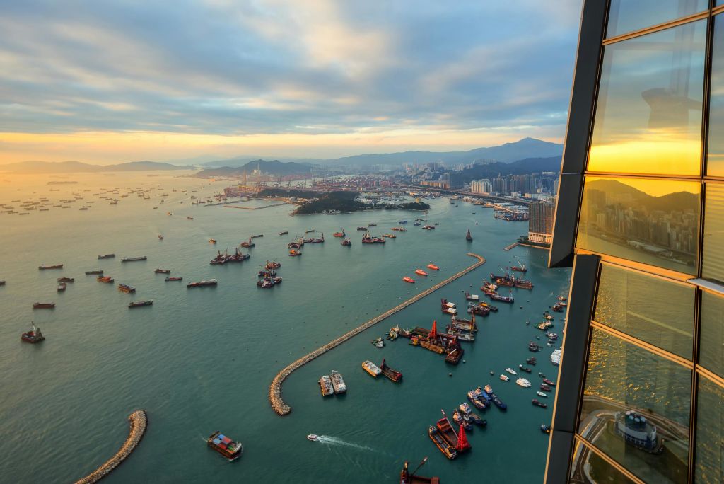 흐린 하늘 아래 도시 풍경과 산으로 둘러싸인 수많은 보트와 배가 있는 분주한 항구의 공중 전망.