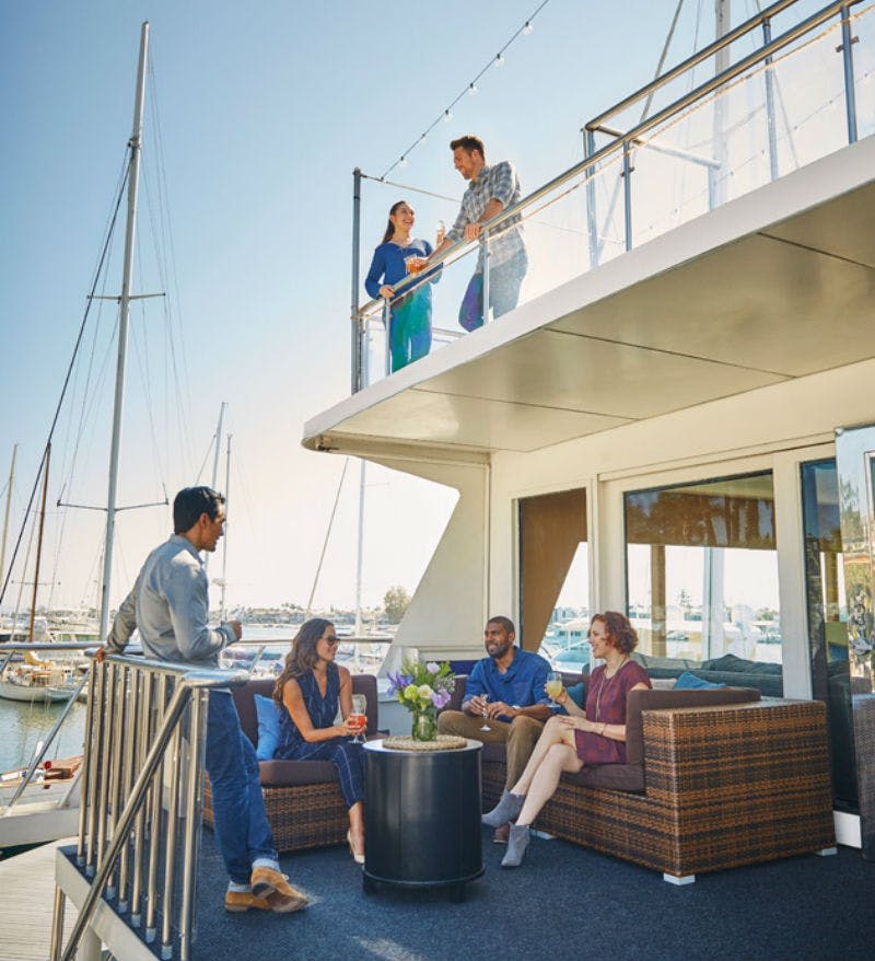 보트에서 휴식을 취하는 사람들. 두 명은 난간으로 상부 갑판에 있고, 네 명은 작은 테이블 주위의 하부 갑판에 앉아 있습니다.