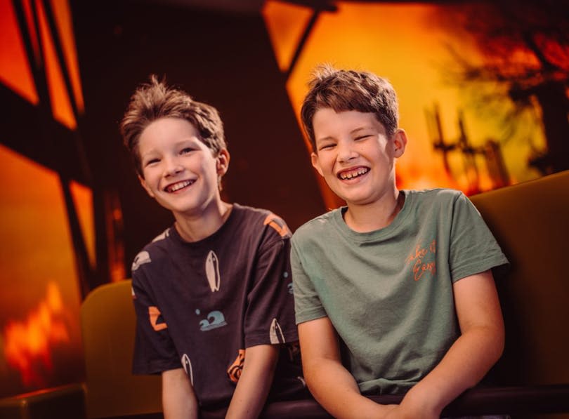 두 명의 어린 소년이 웃고 있습니다. 배경에는 따뜻한 주황색 빛과 추상적인 모양이 있습니다.