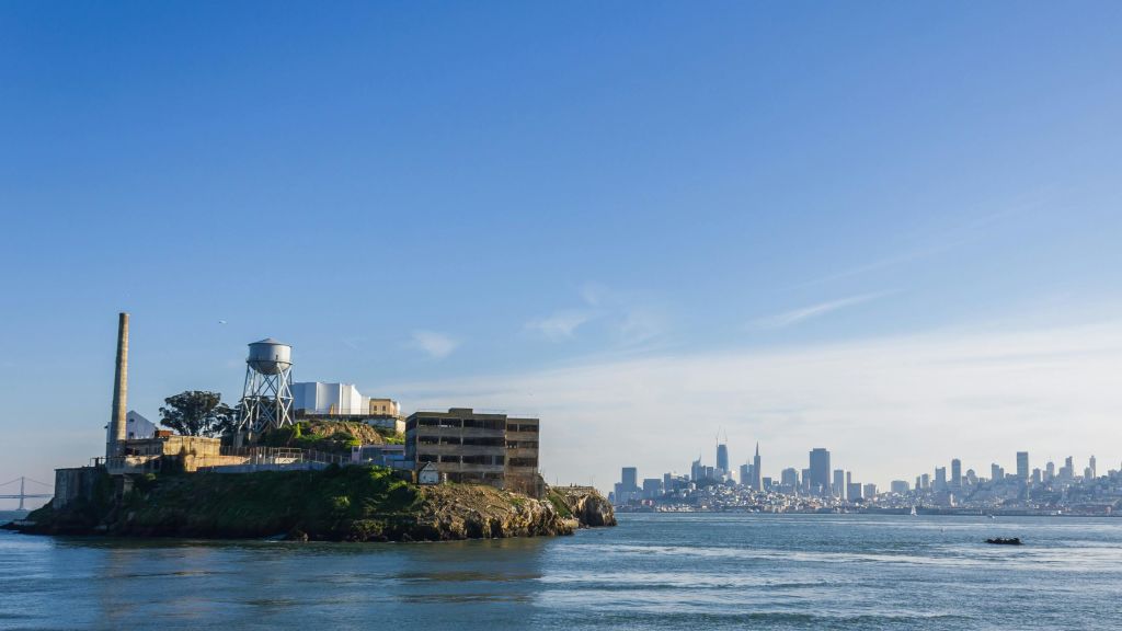 도시의 스카이라인과 푸른 하늘을 배경으로 섬 전경에 낡은 건물과 급수탑이 있습니다.