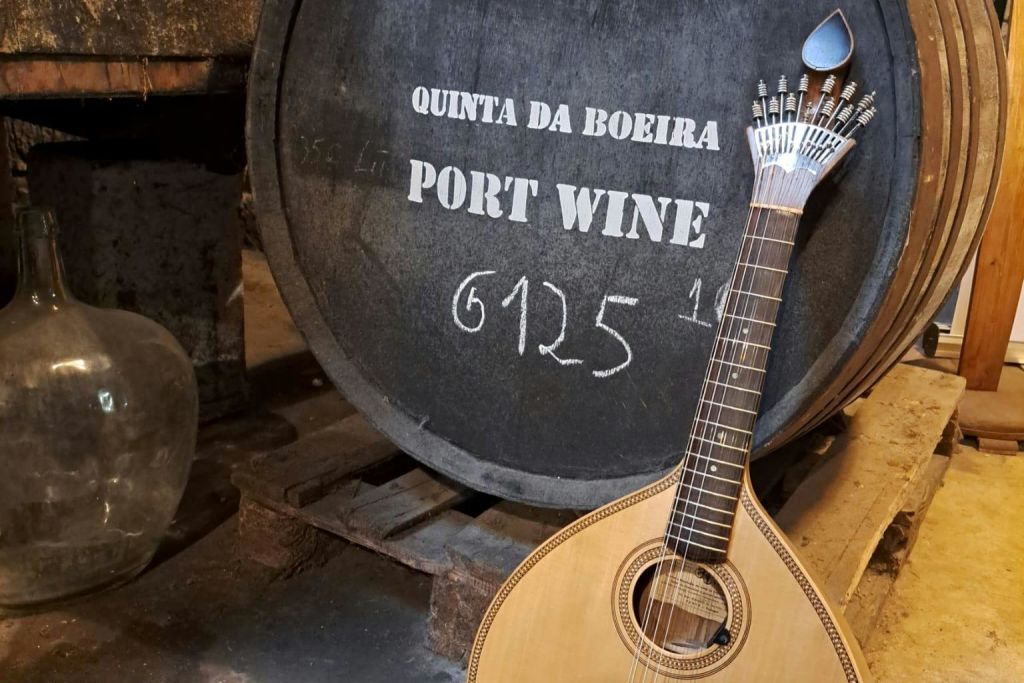 "Quinta da Boeira Port Wine" 이라는 라벨이 붙은 나무 통에 포르투갈 기타가 기대어 있습니다.