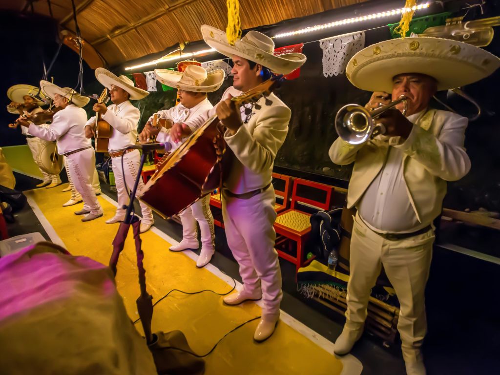 마리아치 밴드는 솜브레로와 함께 전통적인 흰색과 베이지색 의상을 입고 기타와 트럼펫을 연주하며 실내에서 공연합니다.