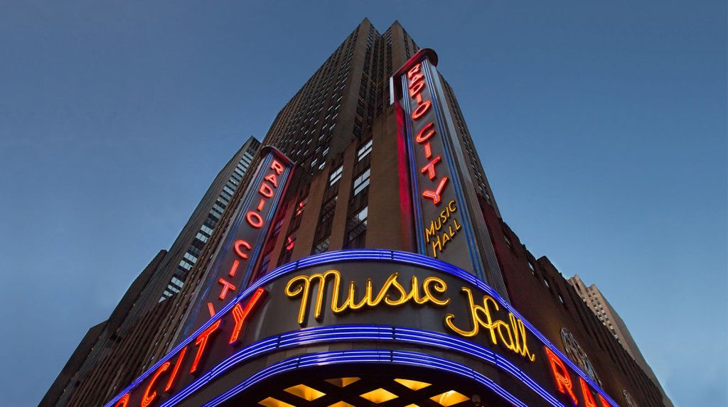 황혼 하늘을 배경으로 "라디오 시티 뮤직 홀" 을 읽는 밝은 네온 사인이 있는 높은 건물.