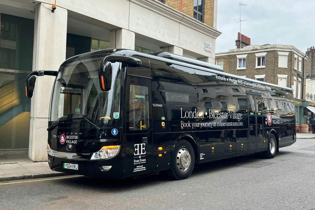 블랙 투어 버스는 "런던 - 비스터 빌리지" 와 그 옆에 여행 서비스를 광고하는 다른 텍스트가있는 도시 거리에 주차되었습니다.