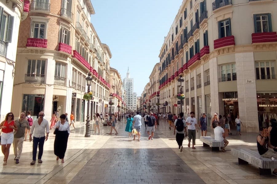 화창한 날 붉은 배너와 발코니로 장식된 건물 사이를 걷는 사람들이 있는 분주한 보행자 거리.