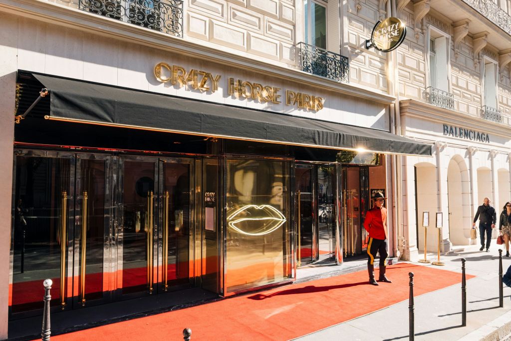 레드 카펫, 빨간색 복장을 한 사람, 유리문에 네온 입술 사인이 있는 크레이지 호스 파리 입구.