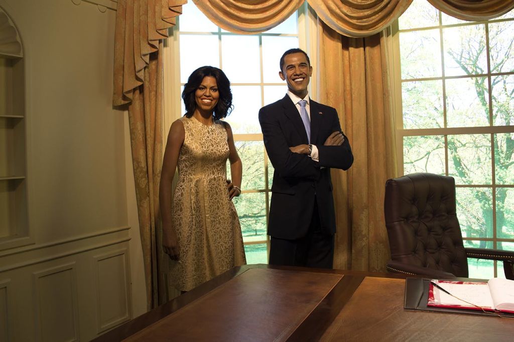 커다란 창문, 복숭아색 커튼, 전면에 나무 책상이 놓인 우아한 사무실에는 미소 짓는 남녀가 서 있습니다.