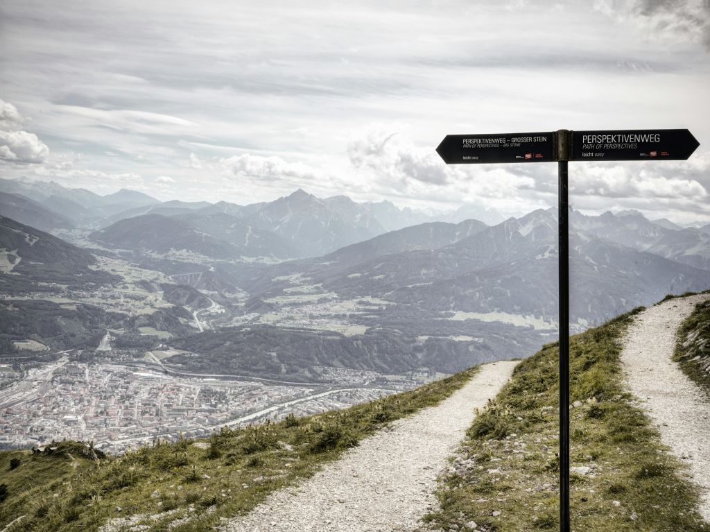 계곡과 마을을 배경으로 먼 산맥이 내려다보이는 등산로를 가리키는 표지판이 있는 산길.