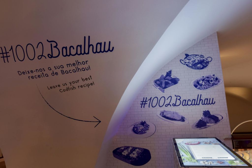 "Bacalhau" 텍스트, 음식 이미지, 해시 태그 및 "최고의 Codfish 레시피를 남겨주세요!" 초대장이 있는 곡선형 흰색 벽.
