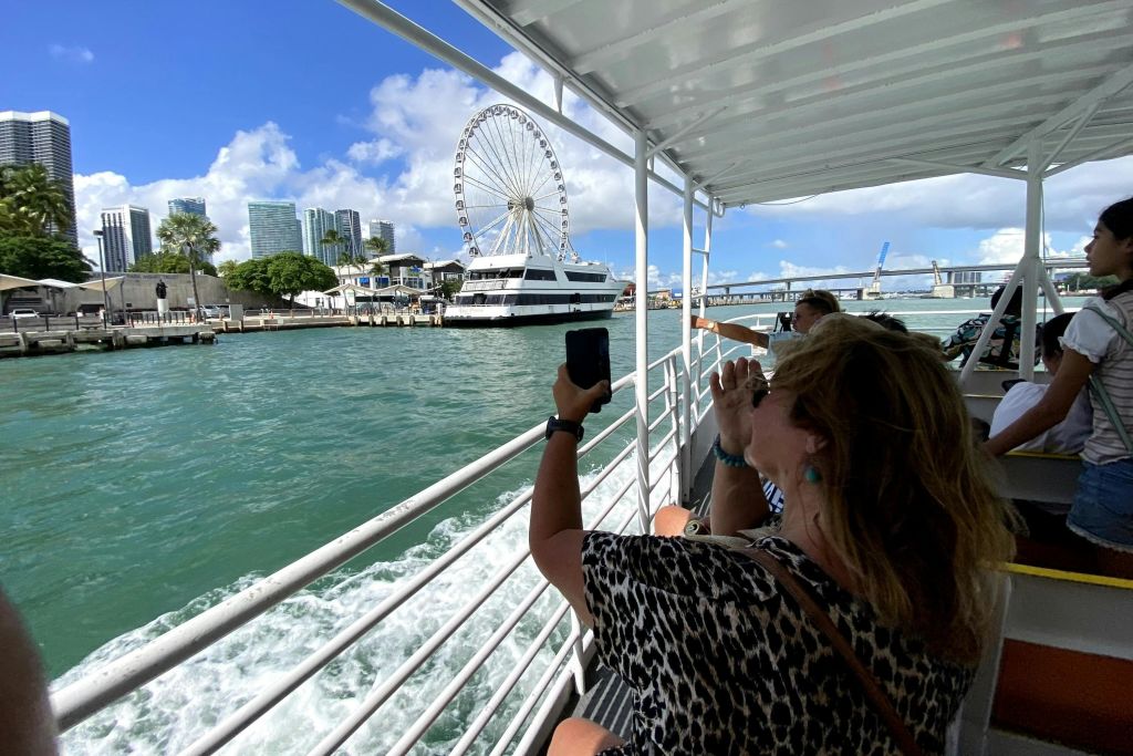 화창한 날 물 건너편에서 대관람차와 건물 사진을 찍는 보트에 탄 사람들.