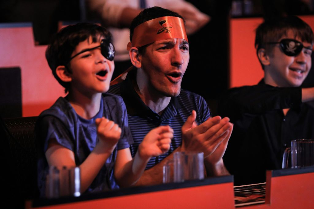 주황색 머리띠를 두른 한 남자와 어린이가 열렬한 환호를 보냅니다. 아이에게도 접안렌즈가 있습니다.