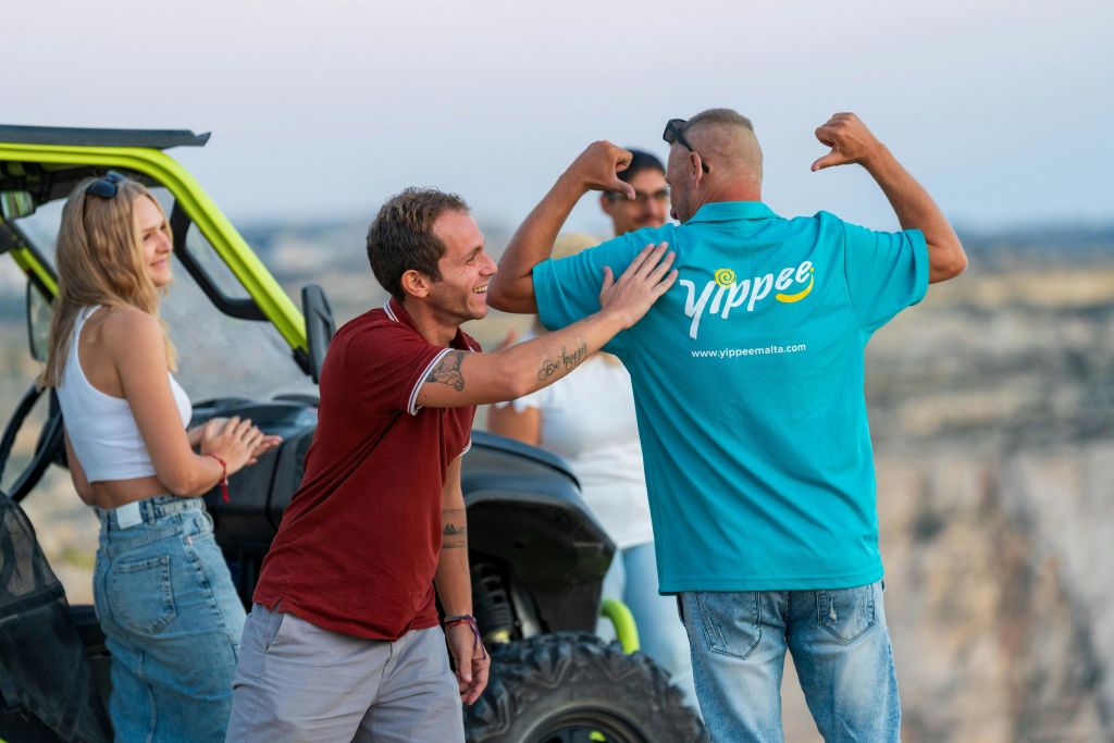 야외에서 오프로드 차량 근처에서 상호 작용하는 사람들의 그룹. 한 사람은 팔을 구부리고 다른 사람은 미소를 짓습니다.