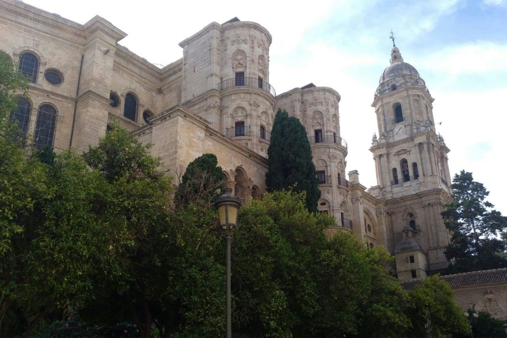녹색 나무와 가로등 기둥으로 둘러싸인 원통형 타워와 아치형 창문이 있는 유서 깊은 석조 건물. 위쪽의 맑은 하늘.