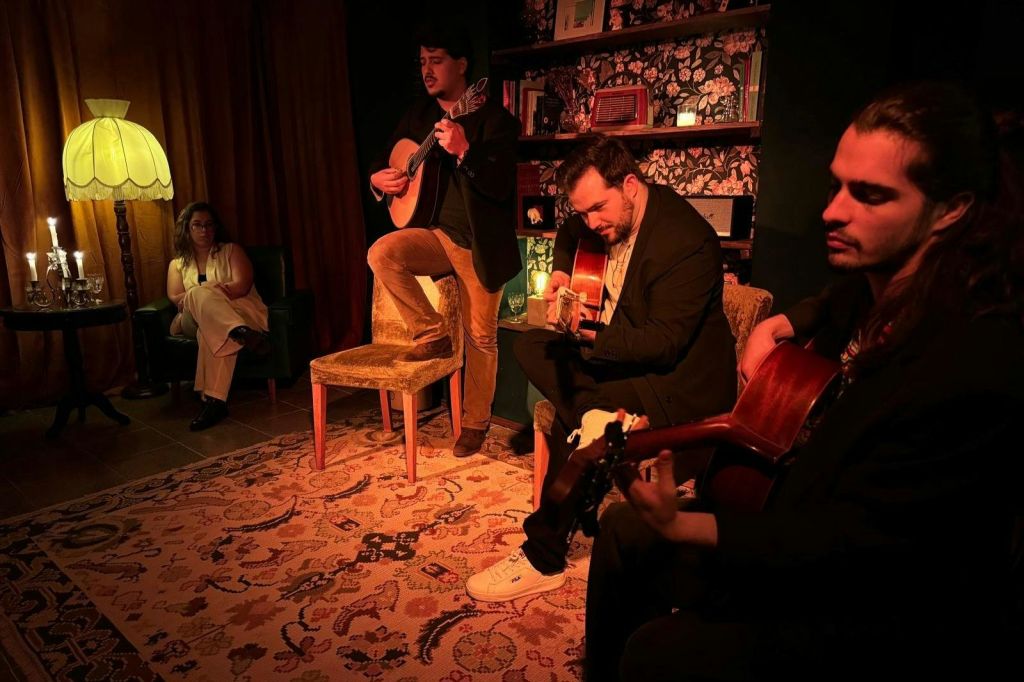 무늬가 있는 러그와 책장을 배경으로 조명이 희미한 방에서 기타를 연주하는 세 명의 남성.