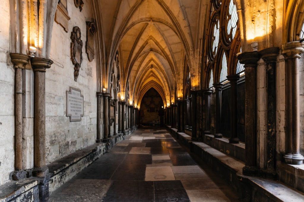 정교한 석조 공예품, 스테인드글라스 창문, 벽면에 플라크가 있는 어두운 조명과 아치형 복도.