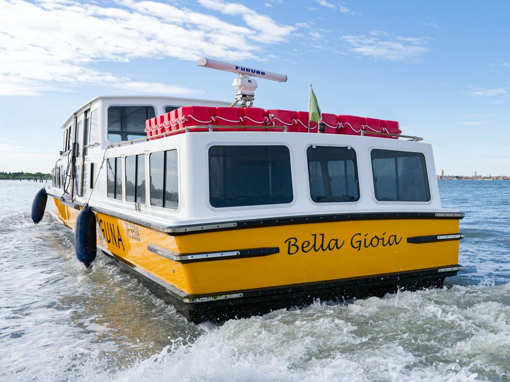 "벨라 지오이아 (Bella Gioia)" 라는 이름의 노란색과 흰색 보트가 구명보트를 타고 부분적으로 흐린 하늘 아래에서 물 위를 유람하고 있습니다.