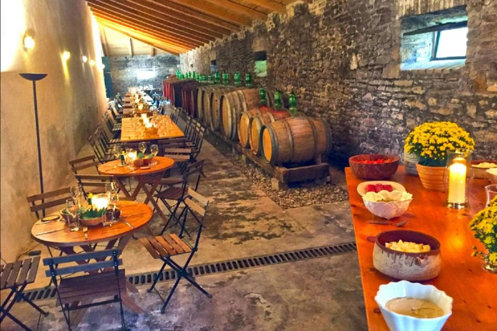 나무 통이 있는 소박한 와인 저장고, 식사용 의자가 놓인 둥근 나무 테이블, 사이드 테이블에 놓인 간식 그릇.