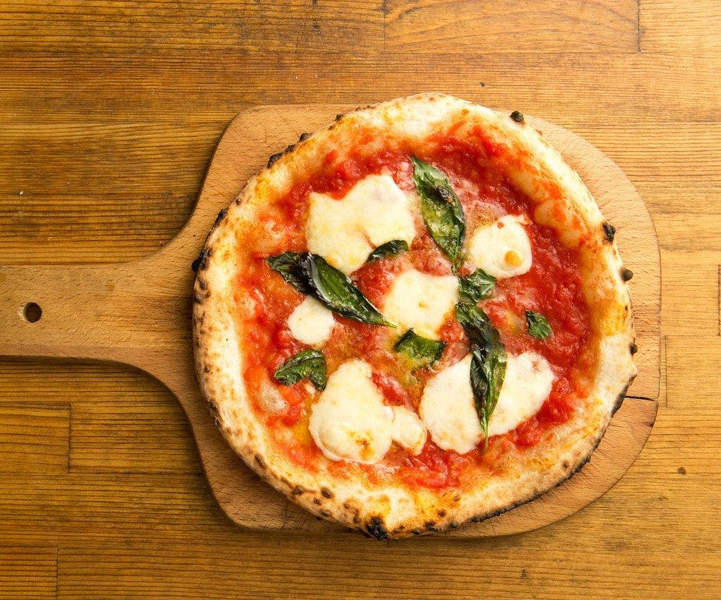 나무 패들에 토마토 소스, 녹인 모짜렐라, 신선한 바질 잎을 얹은 마르게리타 피자.