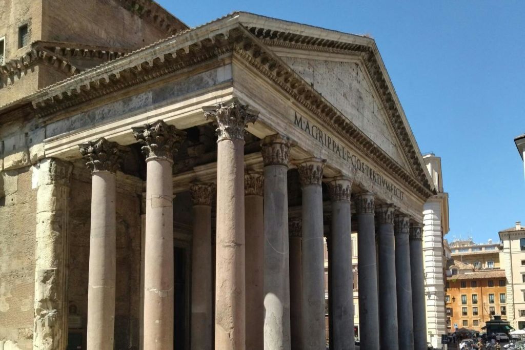 웅장한 기둥과 라틴 문양이 새겨진 페디먼트가 있는 고대 로마 사원은 맑고 푸른 하늘을 배경으로 합니다.