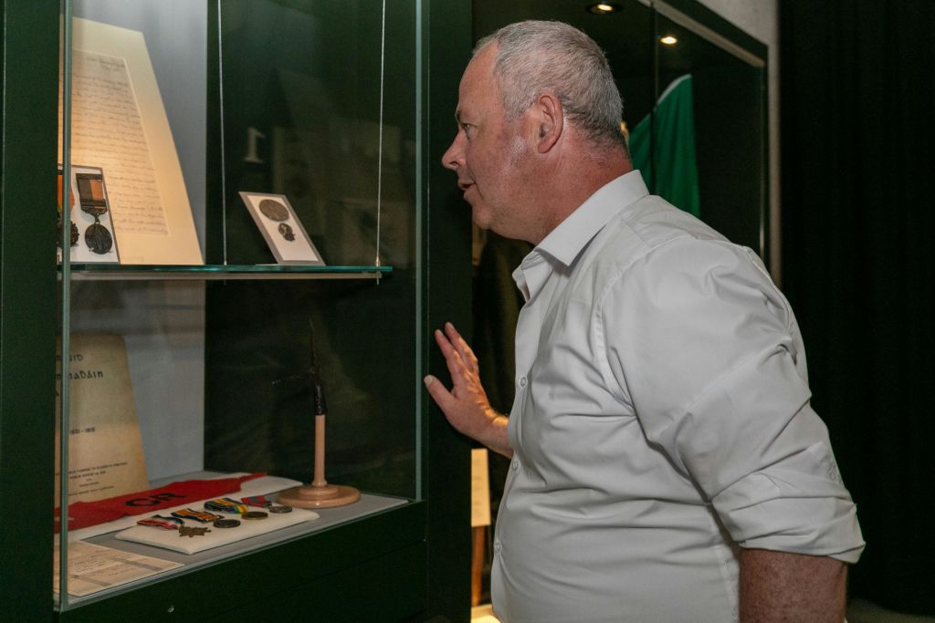 흰색 셔츠를 입은 남성이 박물관에 전시된 물품 (메달과 액자 사진 포함) 을 자세히 살펴보고 있습니다.