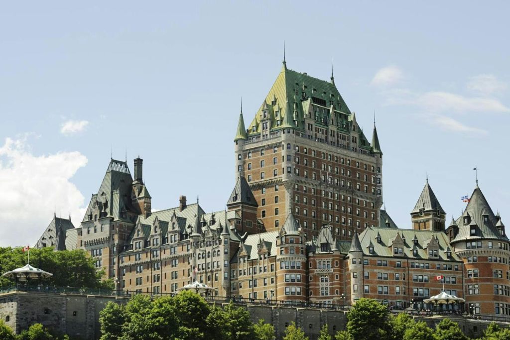 푸른 하늘 아래 나무로 둘러싸인 녹색 지붕과 첨탑이 있는 커다란 역사적인 건물.