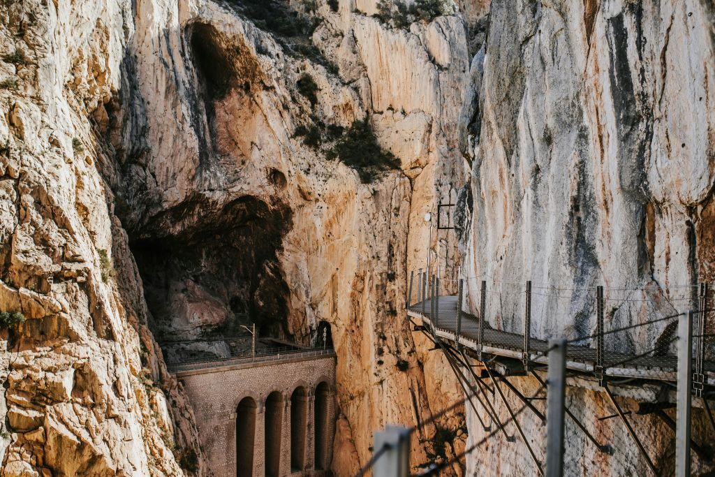 바위 협곡에 아치가 있는 다리가 내려다보이는 가파른 바위 절벽에 난간이 달린 좁은 통로.
