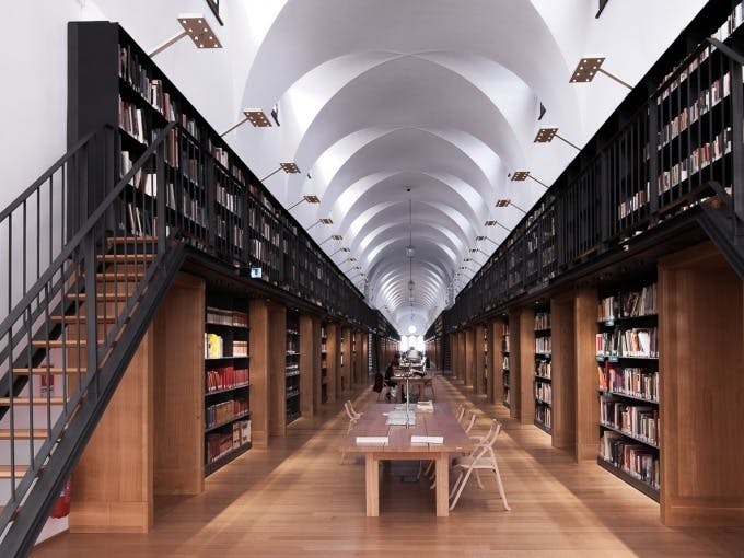 높은 천장, 나무 바닥, 독서대, 책 선반이 양쪽에 있는 길고 아치형 도서관입니다.