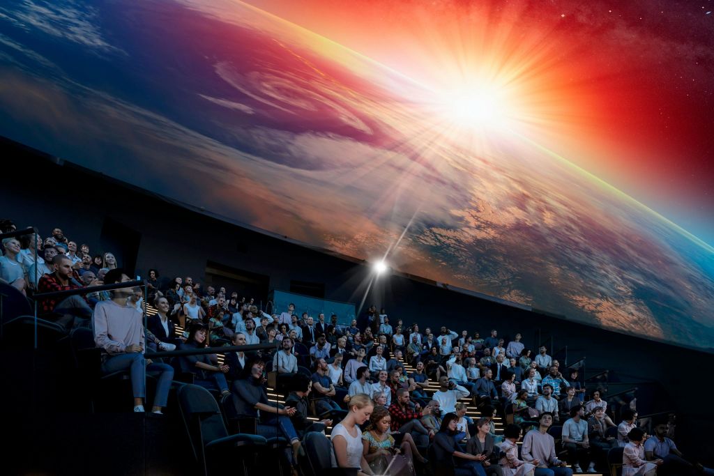 많은 청중이 천문관에 앉아 지구 위 석양의 생생한 투영을 관찰합니다.