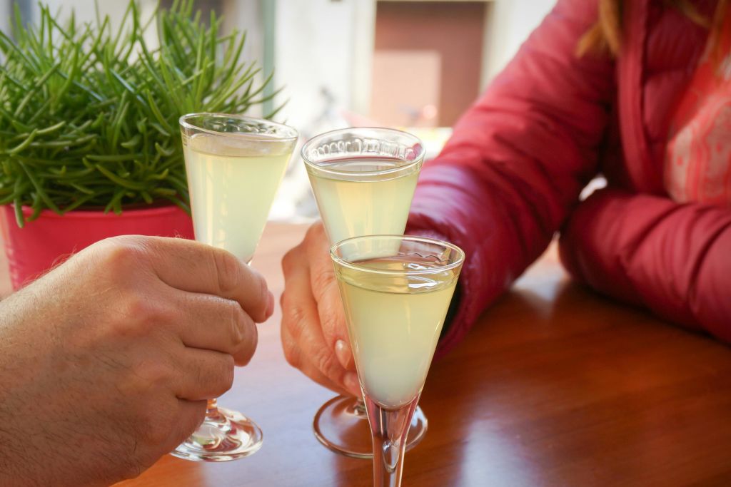 녹색 식물 근처의 나무 테이블 위에 두 사람이 담황색 음료를 담은 잔 세 개.