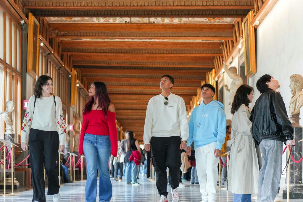 측면을 따라 나무 대들보와 조각상이 있는 복도를 걷는 세 사람. 통로는 밝고 붐빕니다.