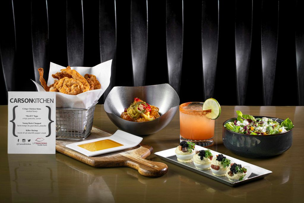 프라이드 치킨, 파스타 한 그릇, 라임 칵테일, 샐러드, 데블드 에그, 디핑 소스가 포함된 테이블입니다.