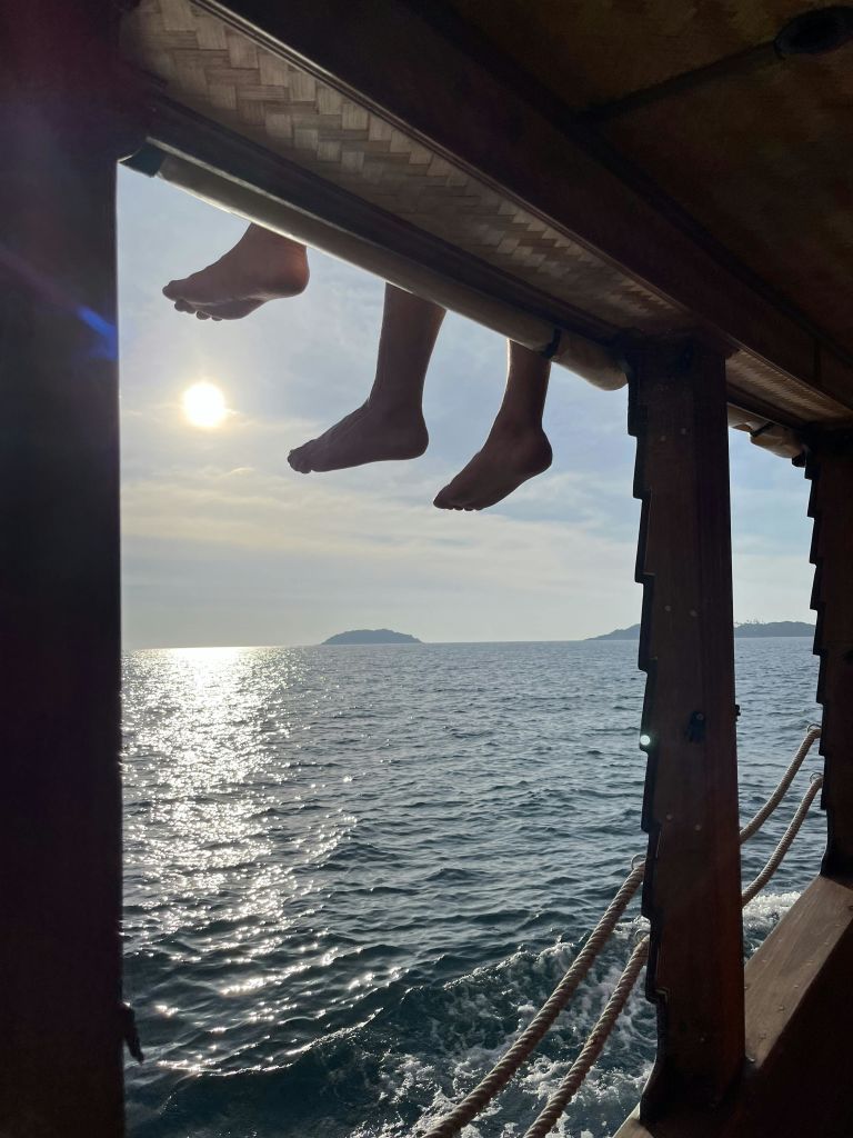 밝은 태양과 먼 섬을 배경으로 바다가 내려다보이는 목조 구조물에서 두 쌍의 발이 매달려 있습니다.