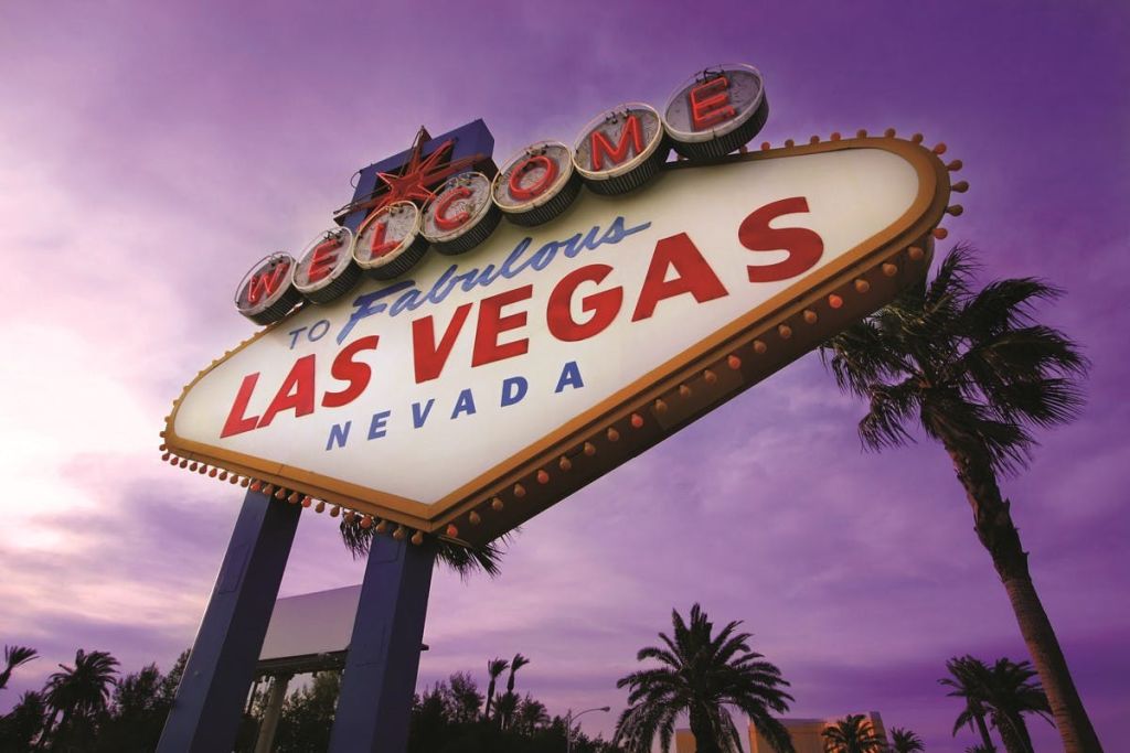 보라색 하늘 아래 야자수를 배경으로 "Welcome to Fabulous Las Vegas, Nevada" 표지판을 비춥니다.