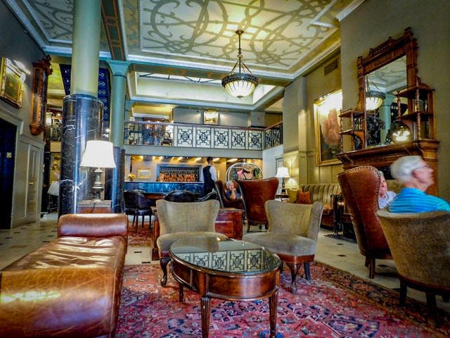 가죽 의자, 화려한 천장, 샹들리에, 바를 배경으로 한 세련된 라운지 공간입니다.