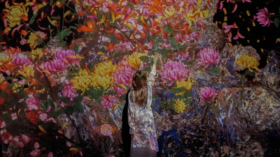 밝은 색상의 옷을 입은 사람이 꽃과 녹음의 생생하고 화려한 벽 투영에 손을 뻗습니다.