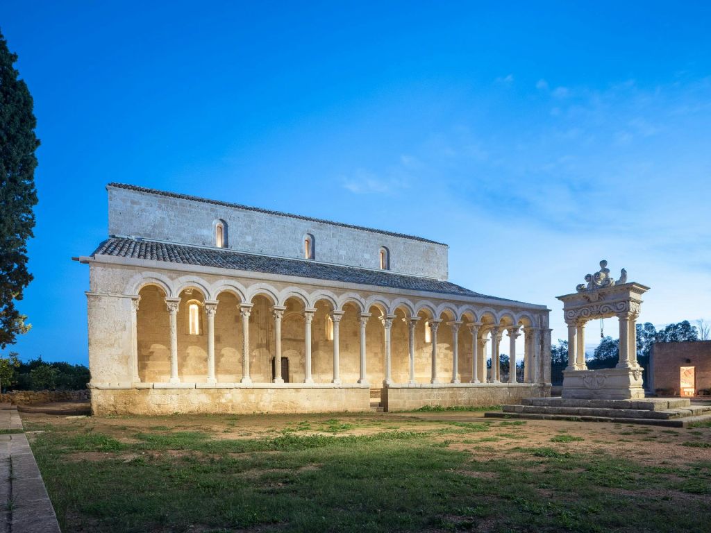 맑고 푸른 하늘 아래 아치형 기둥과 내부 조명이 있는 고대 석조 건물로 오른쪽에 장식 구조물이 있습니다.