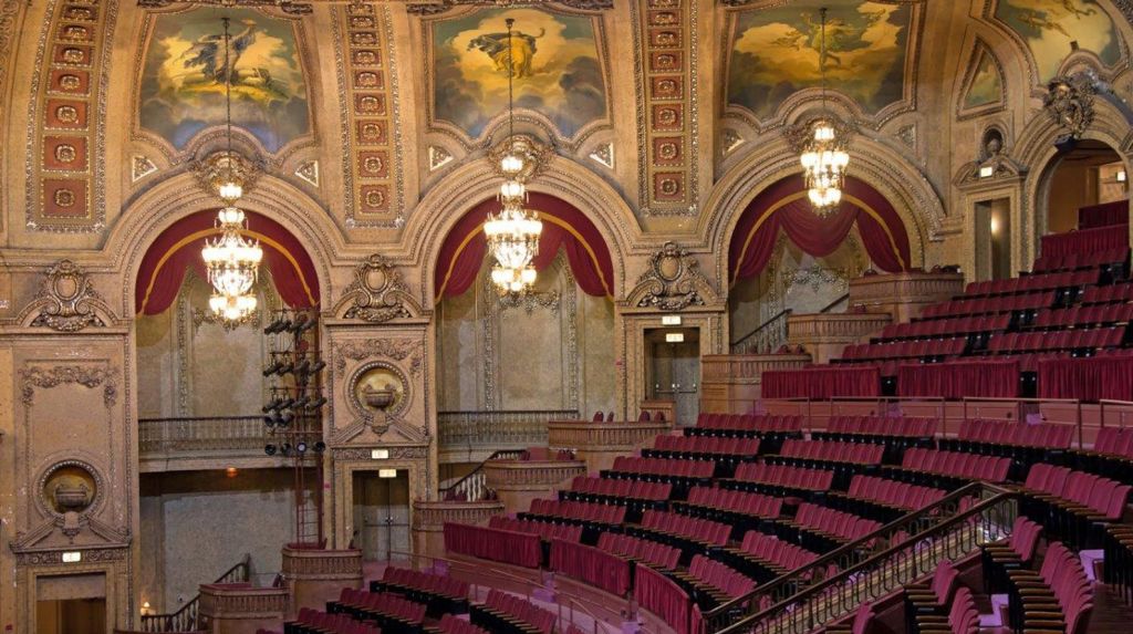 레드 벨벳 시트, 샹들리에, 장식 아치, 페인트 천장 벽화로 장식된 화려한 극장 내부.
