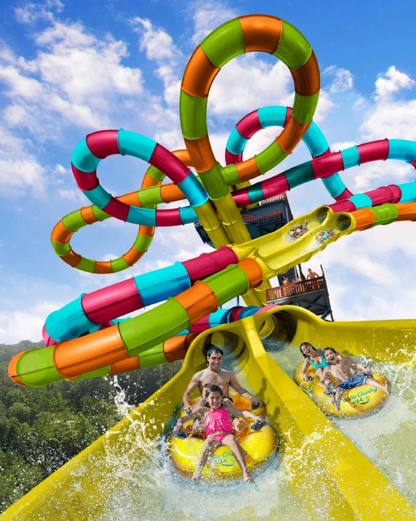 노란색 팽창식 뗏목을 타고 튜브가 얽힌 다채로운 워터 슬라이드를 따라 내려가는 사람들은 바닥에 물방울을 만듭니다.