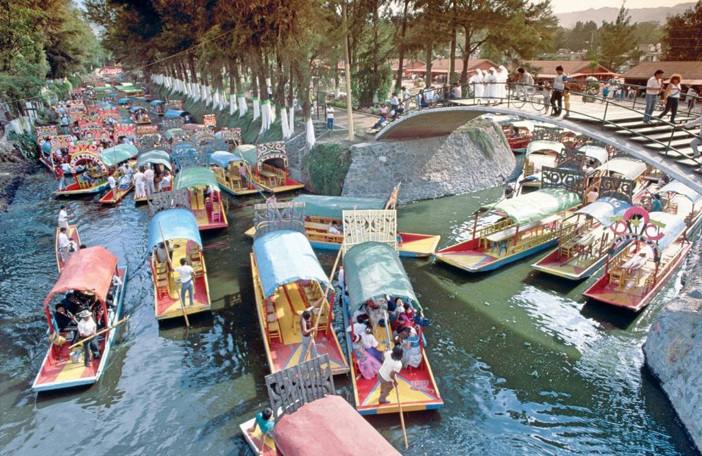 돌다리 아래 운하에 캐노피가 달린 화려한 보트가 다리와 보트의 나무와 사람들로 둘러싸여 있습니다.