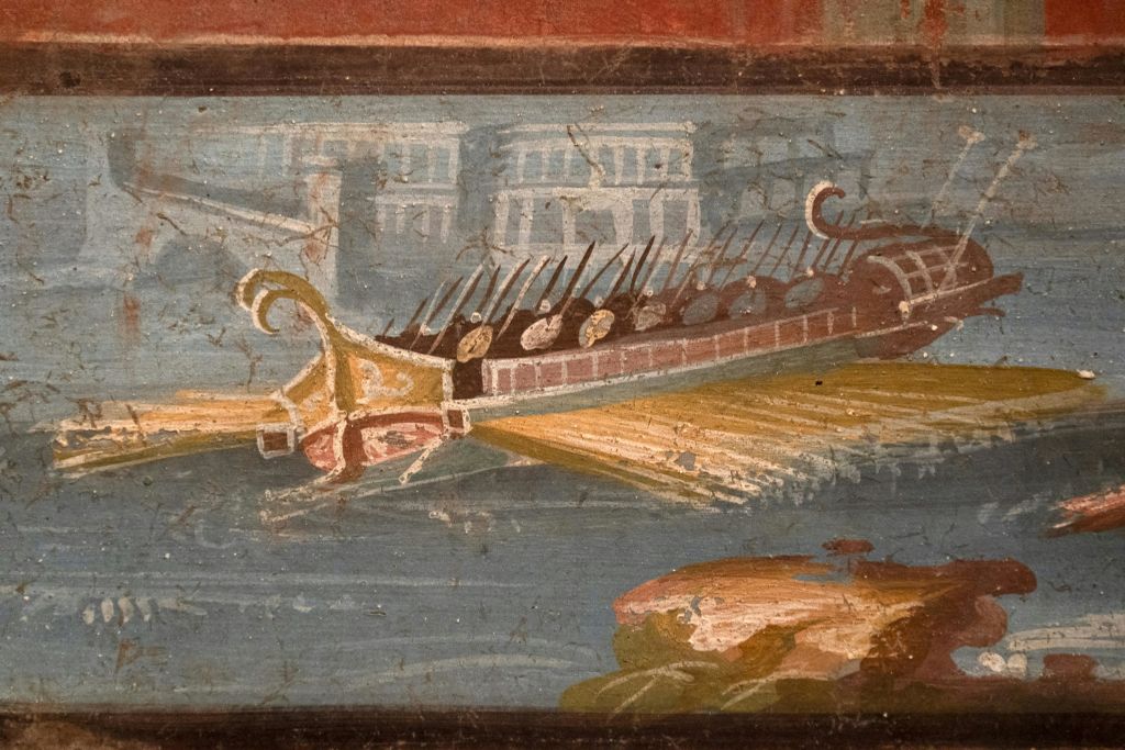 고대 프레스코화는 로마 군함이 노를 젓고, 물 위를 항해하며, 건물을 배경으로 오른쪽에 착륙하는 모습을 묘사하고 있습니다.