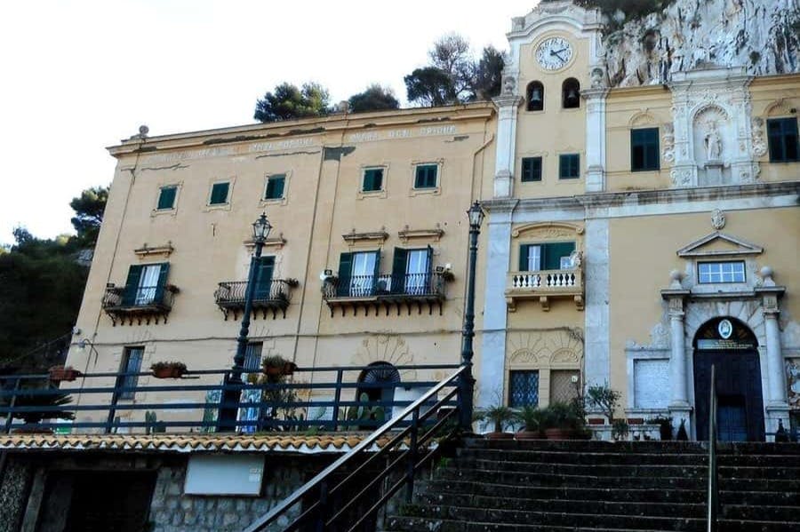 나무와 관목으로 둘러싸인 시계탑, 발코니, 계단이 있는 역사적인 건물입니다.