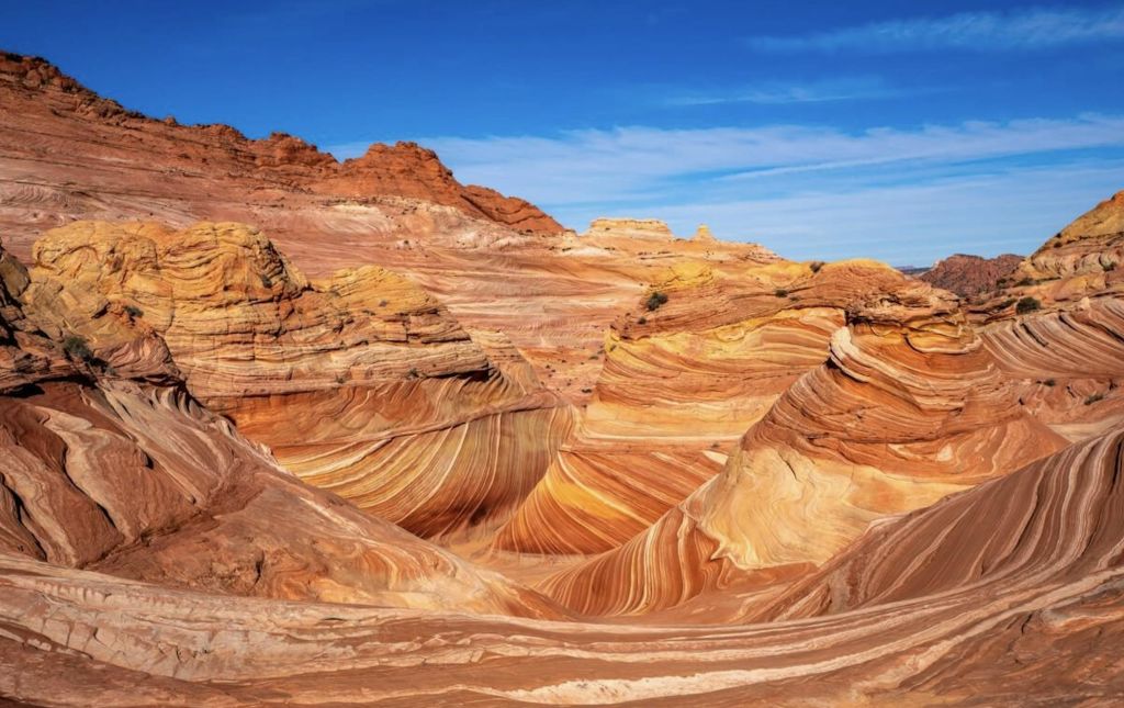 빨간색, 주황색, 노란색, 흰색 층의 소용돌이치는 패턴으로 맑고 푸른 하늘 아래 다채로운 사암 암석이 형성되어 있습니다.